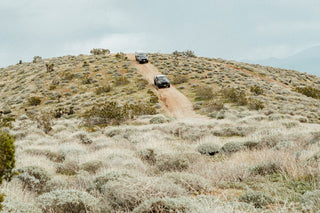 Two trucks coming over a ridge in the desert.