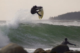 A surfer launches an air while his friend looks on.