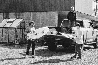 Surfers putting their surfboards in a truck bed.