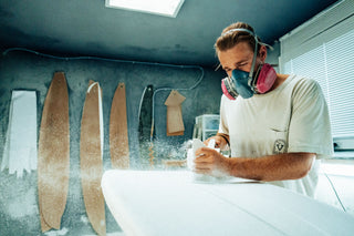 A surfboard shaper using a planer to shape a surfboard.