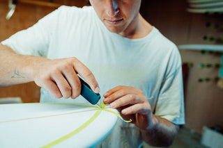 A surfboard shaper cutting tape with his Palmer utility knife. 