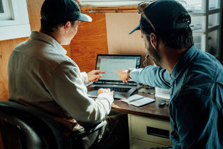 A surfboard shaper and a surfer designing a board on a computer with CAD software.