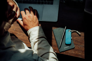 A person works on a laptop with a utility knife, edc pen, and notebook at hand.