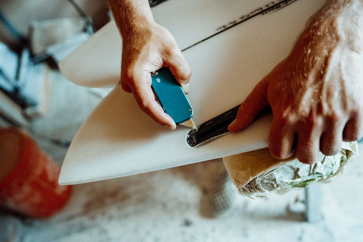 A surfboard shaper using his Palmer utility knife to remove damaged fiberglass on a surfboard.