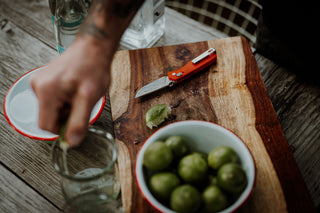 A man squeezing lime juice into a glass after slicing the lime with his knife.